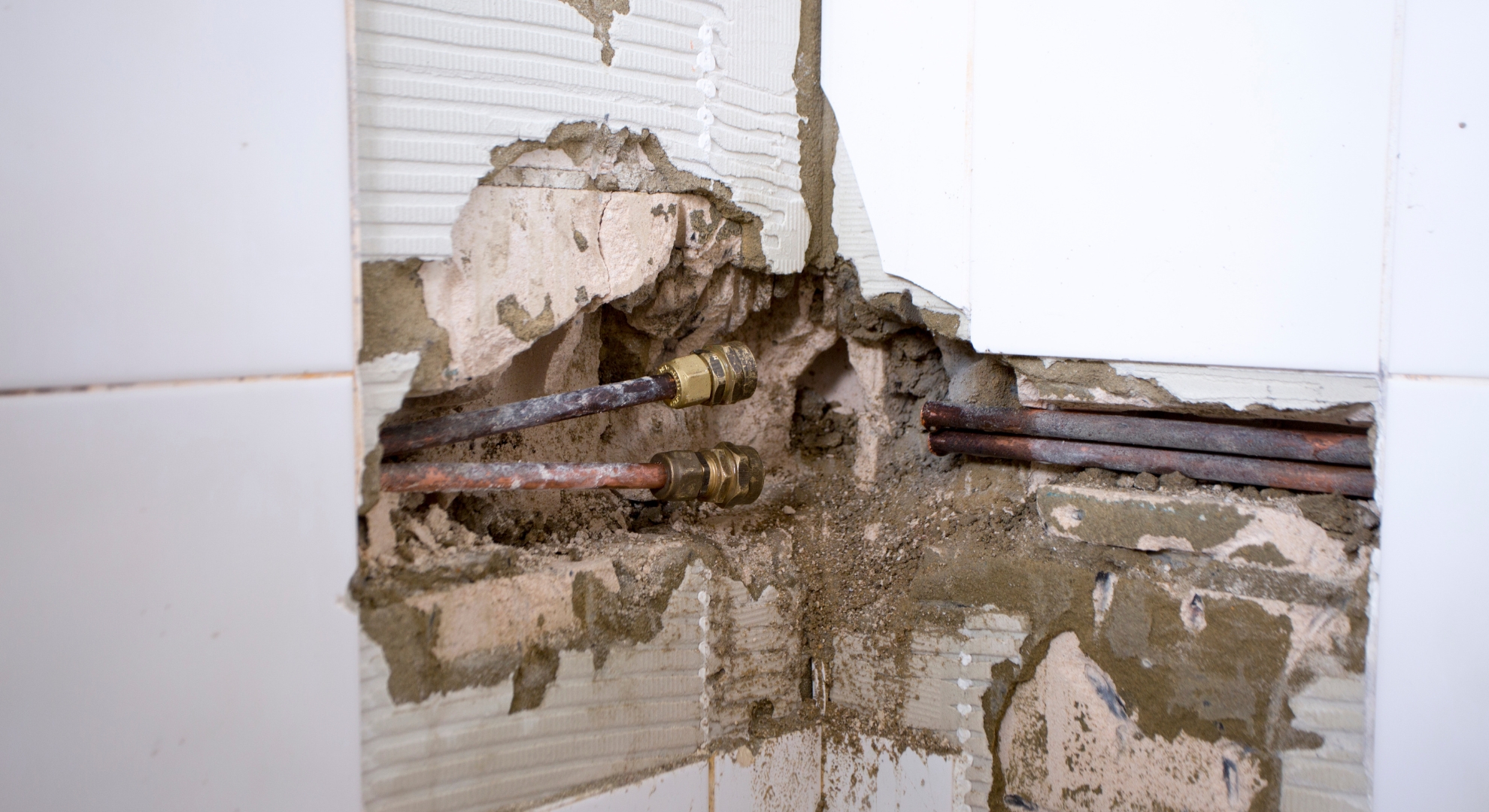 Copper plumbing pipes revealed behind broken wall tiles during a bathroom renovation project.