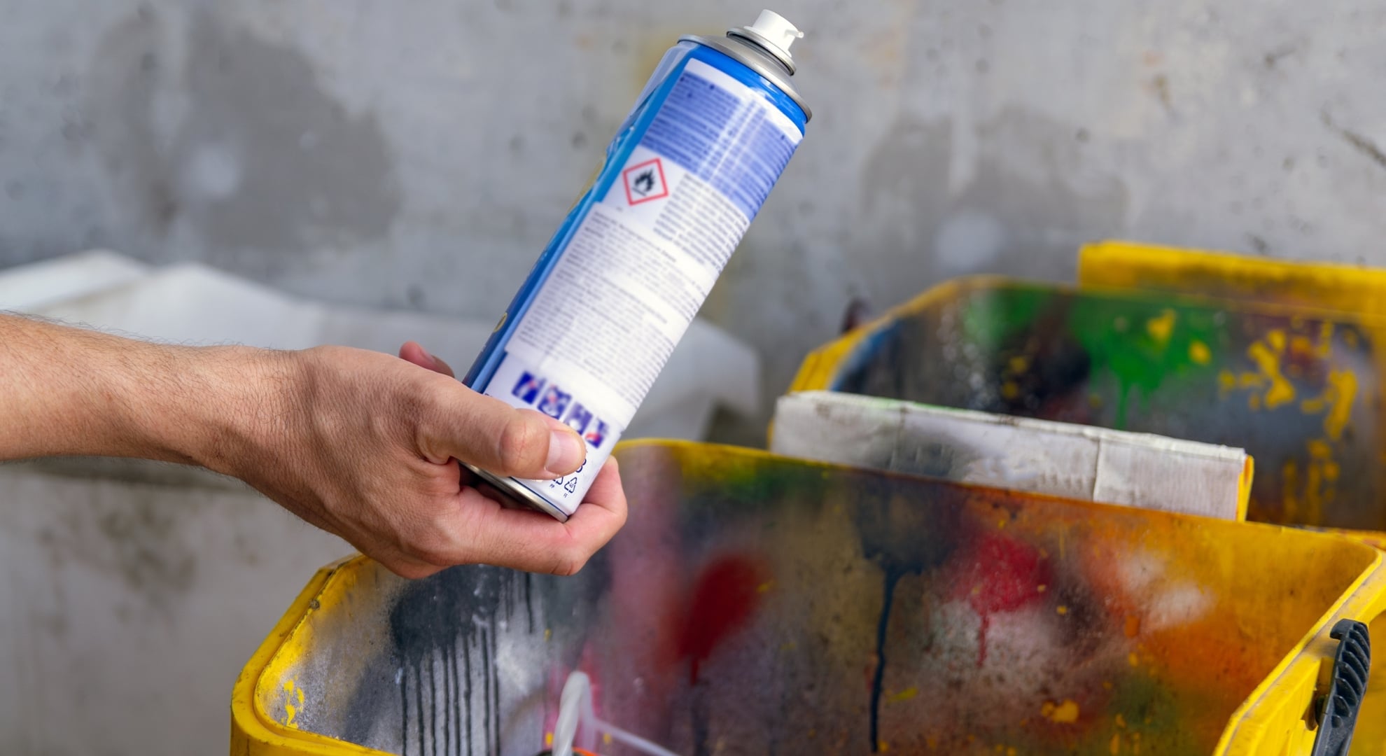 Person properly disposing of a household chemical spray can into a dedicated disposal container.