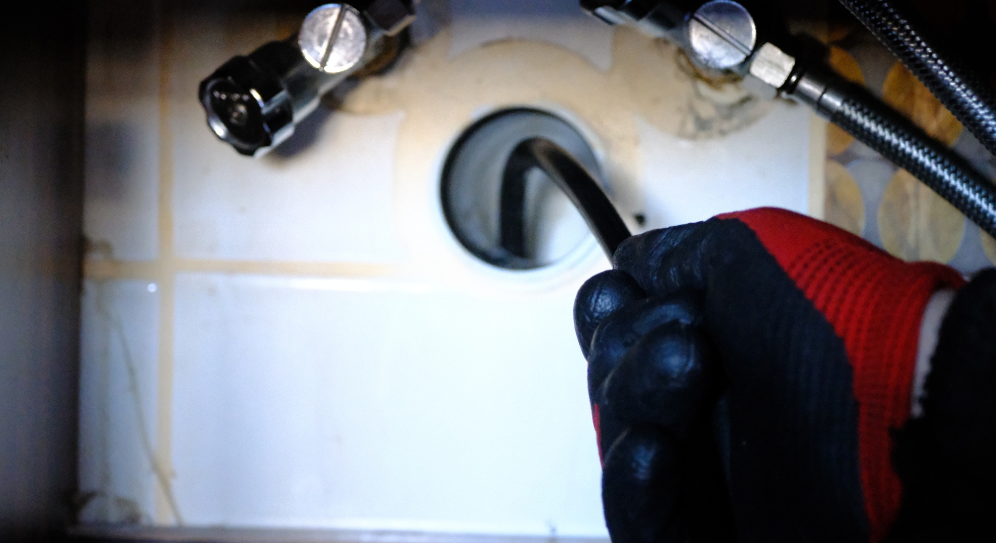 Plumber using a plumbing snake camera cable to inspect a pipe under a sink.